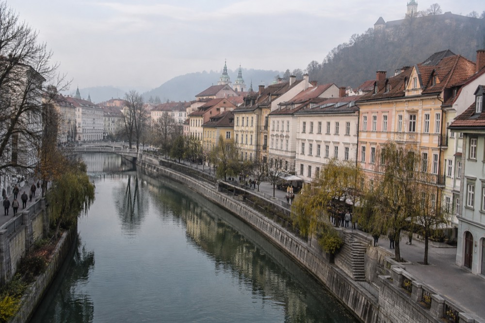 Pastel buildings and a riverside promenade in Ljubljana old town under a soft sky