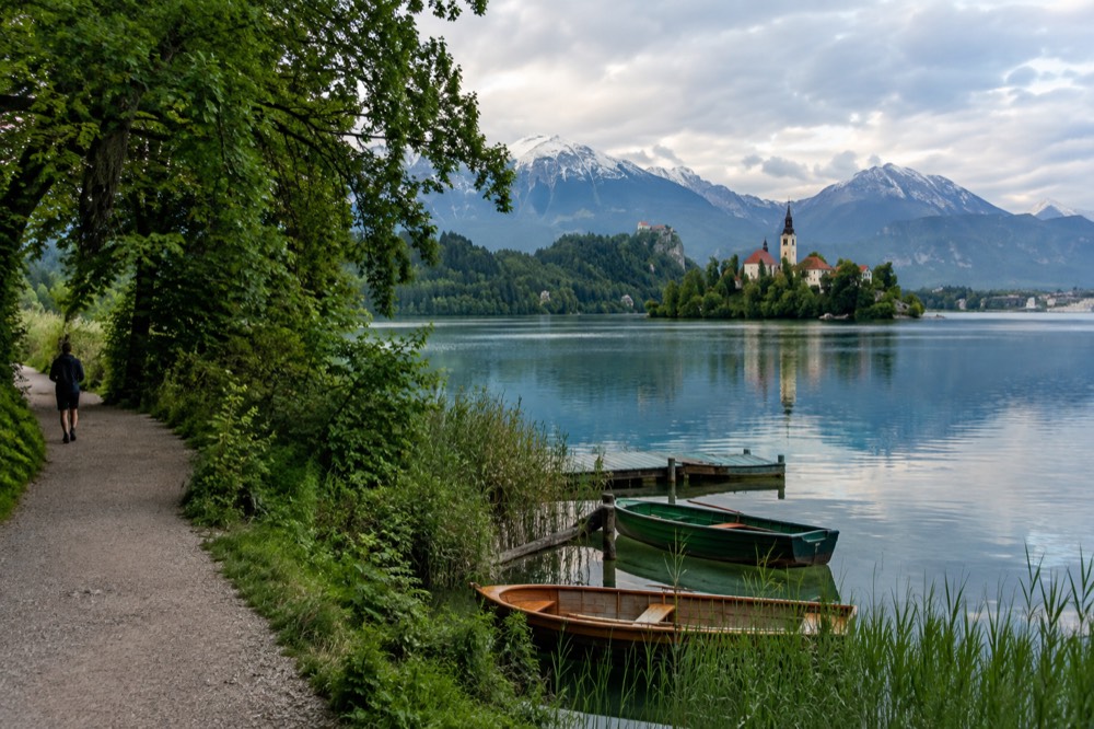 A quiet stretch of the Lake Bled shore path with small boats moored near the reeds