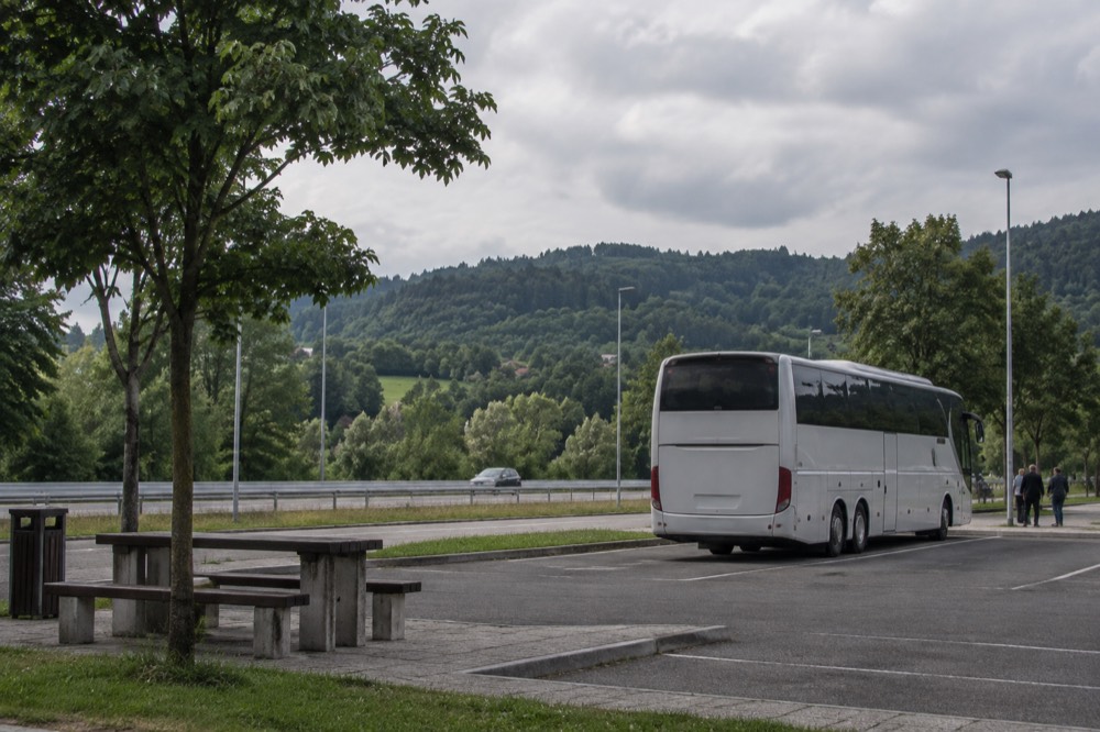 A coach parked at a border-area rest stop with green hills behind it