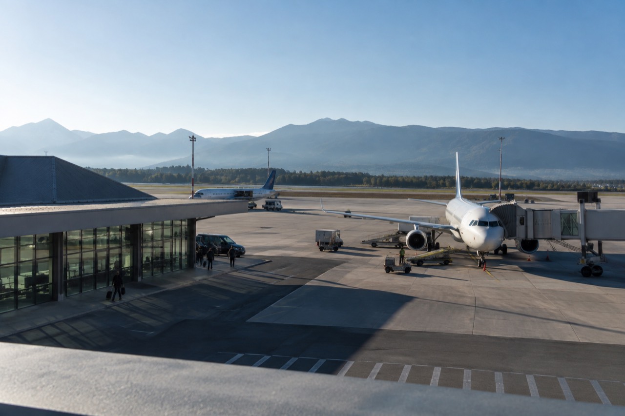 A small regional airport terminal building under a blue sky with parked aircraft on the apron