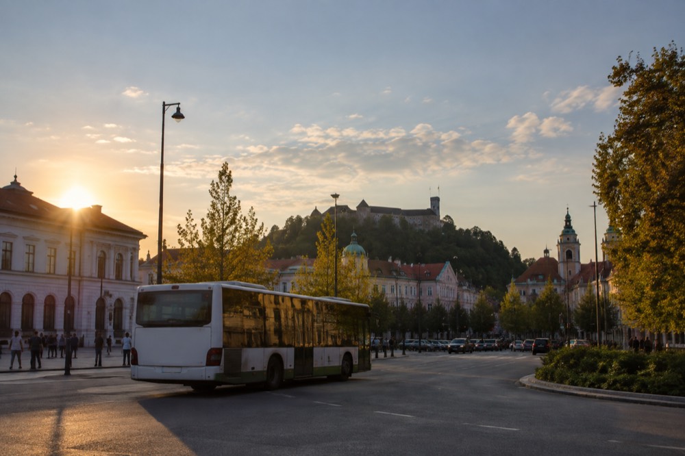 A bus pulling out of Ljubljana's main station forecourt with the city skyline behind