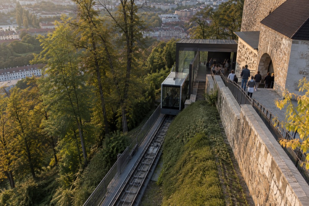 Visitors boarding the funicular at the upper station beside the castle courtyard wall in late afternoon light