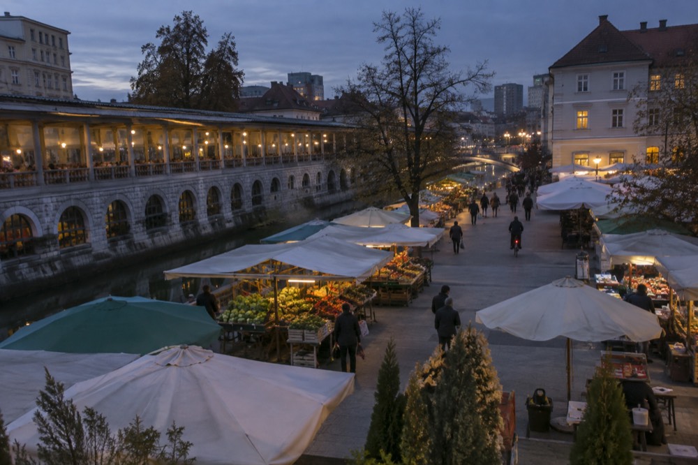 A pedestrian square with market umbrellas and cyclists passing through