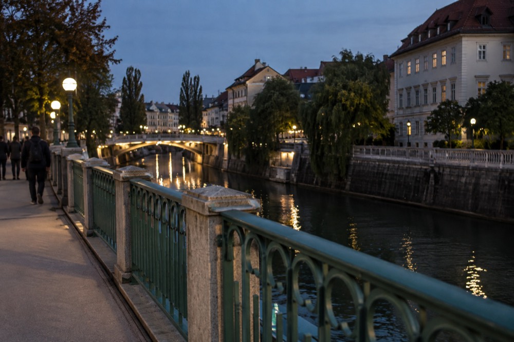 Evening view of a lit bridge with dragon statues and riverside buildings reflected in water