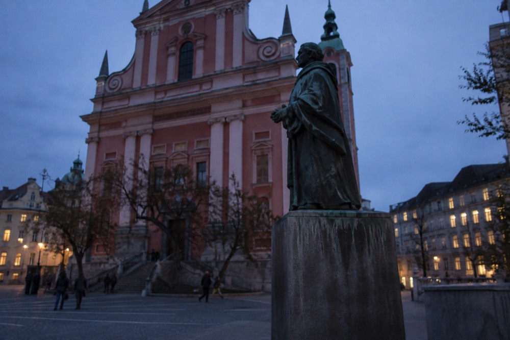 A bronze statue on a plinth at the edge of the square, the church facade rising behind it