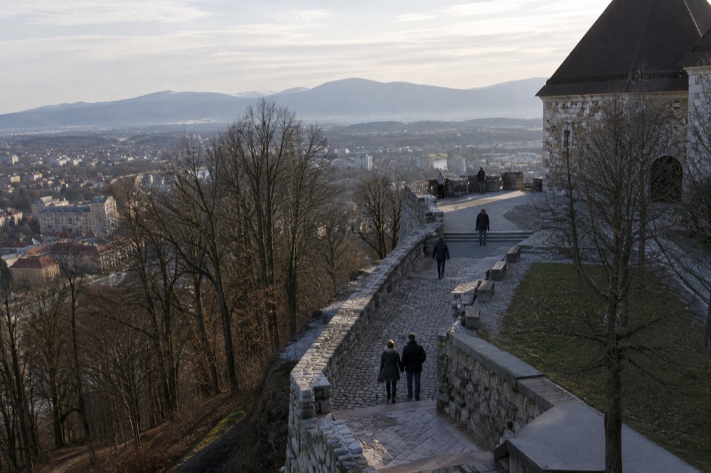 A stone rampart walkway overlooking rooftops and distant mountains
