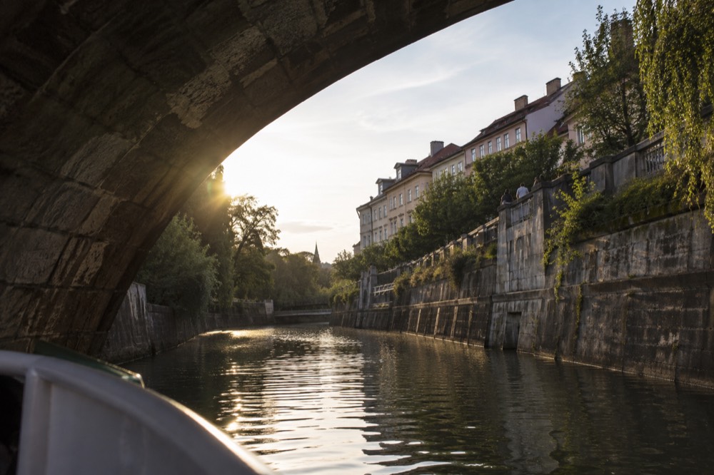 View from a river boat passing under the stone arch of an old Ljubljana bridge with facades on both banks