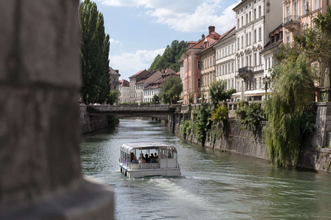 A small passenger boat cruising the Ljubljanica river past the pastel facades and bridges of Ljubljana old town