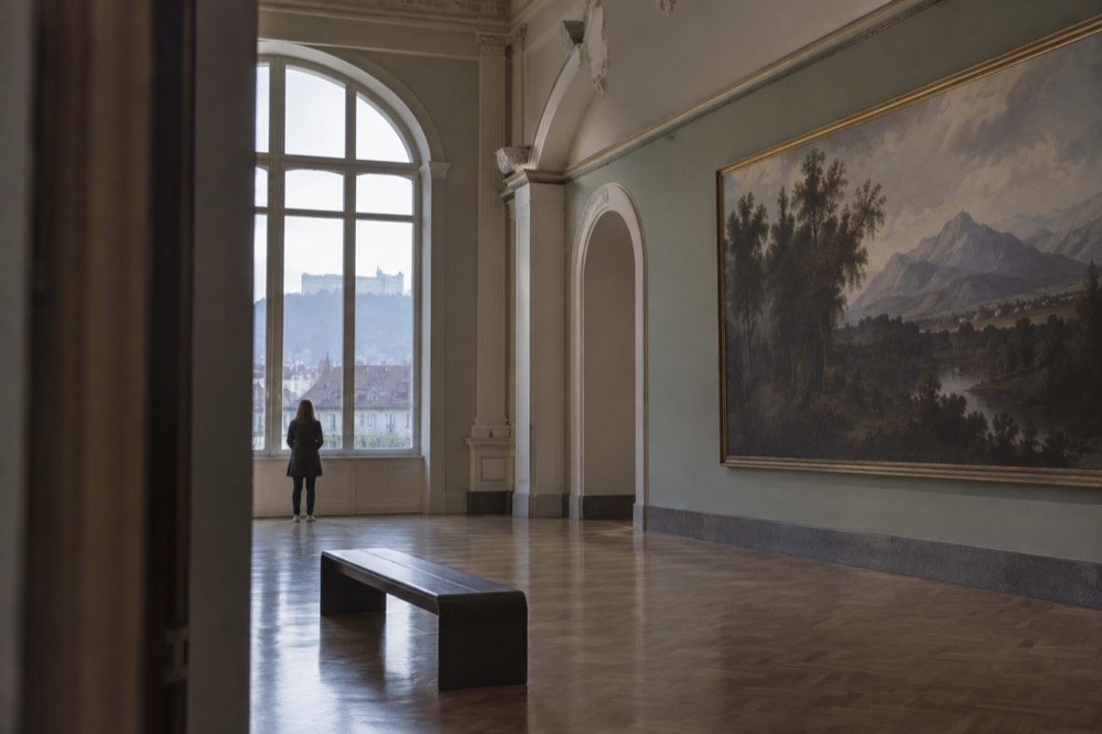 Gallery room with large landscape paintings of mountains and lakes on the walls