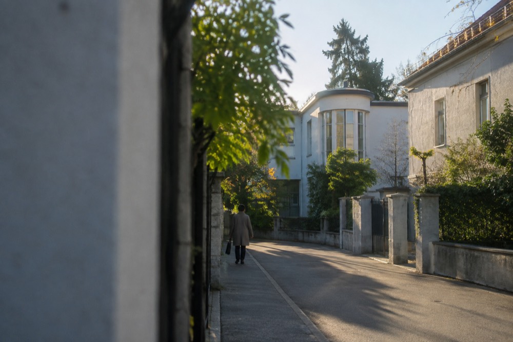 A quiet residential street of low houses with the round corner window of a white villa at the far end