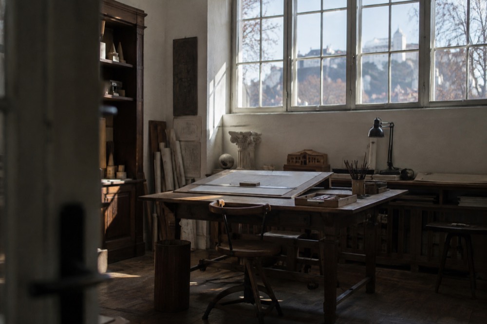 An architect's studio with a wooden drawing board, shelves of instruments and daylight from a high window