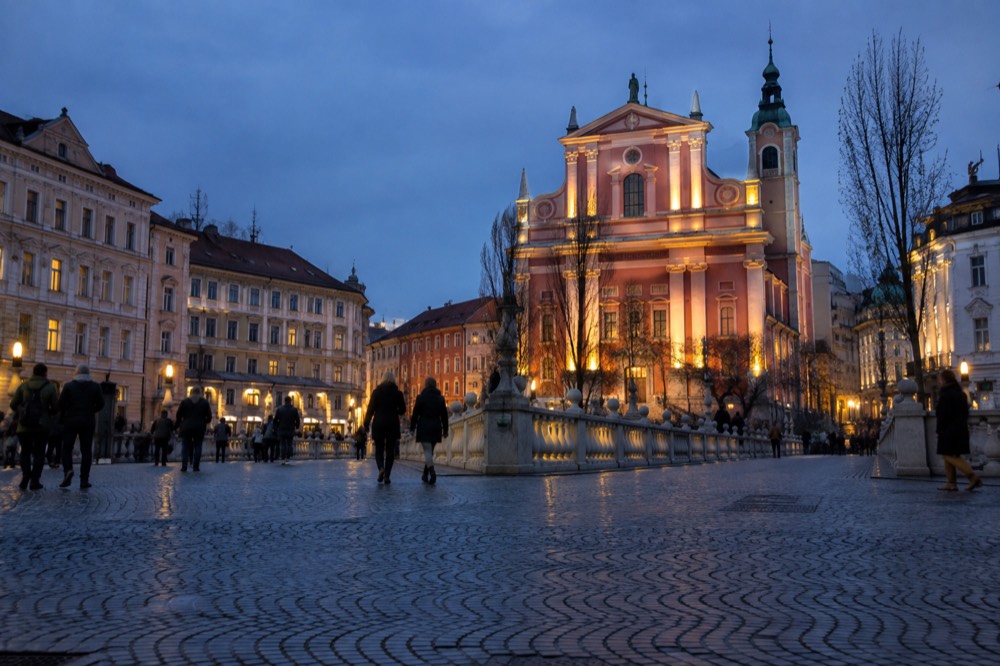 Evening view of a lit church facade above a river bridge in a European city