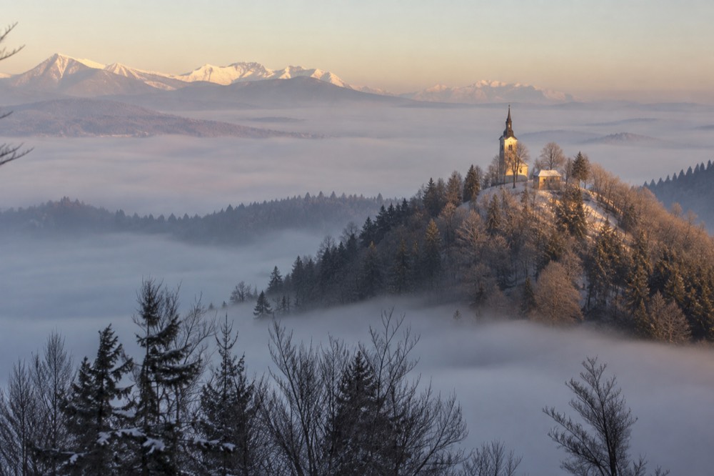 A frosty hilltop church at dawn with warm light on the summit and fog in the valley