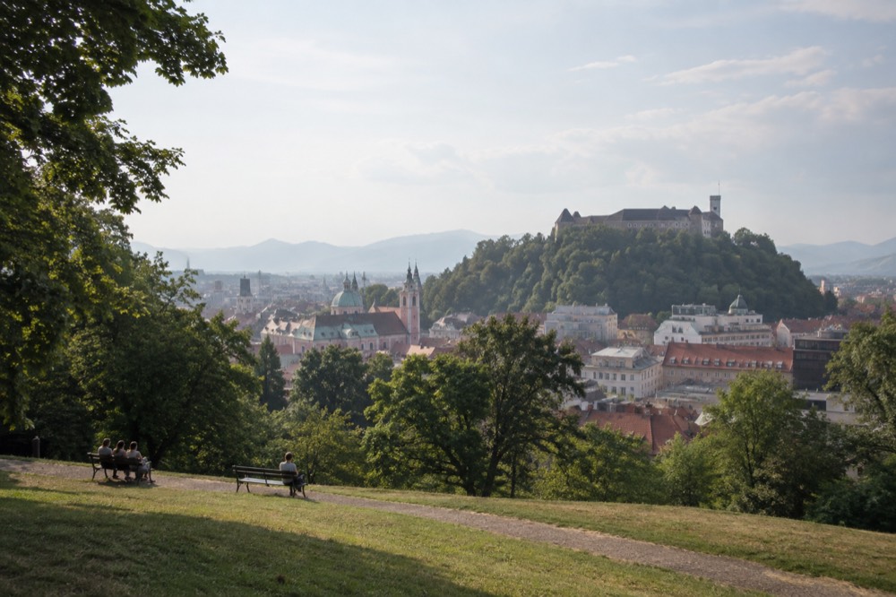 View from a park hillside over rooftops toward a castle on a wooded hill