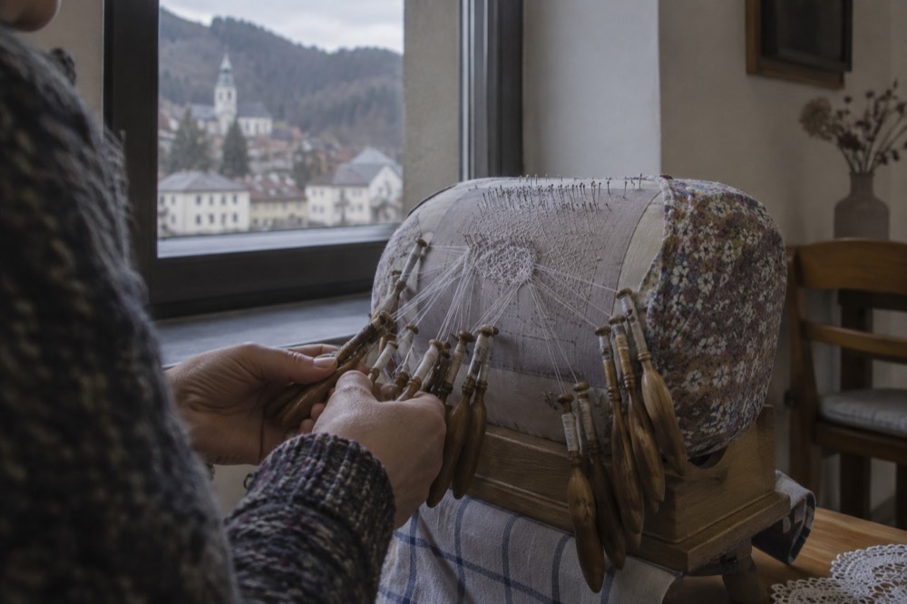 a lacemaker's hands working bobbins on a cushion with fine white thread