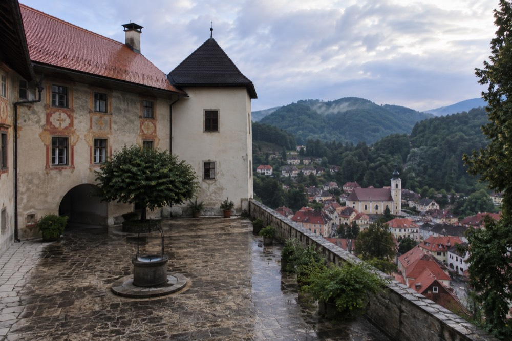 a castle courtyard with painted facades above a small town of red rooftops
