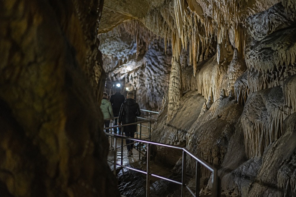 a lit underground cave passage with stalactites above a walkway