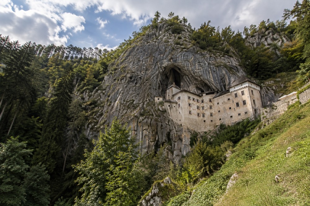 Predjama Castle built into a cliff face above green woodland