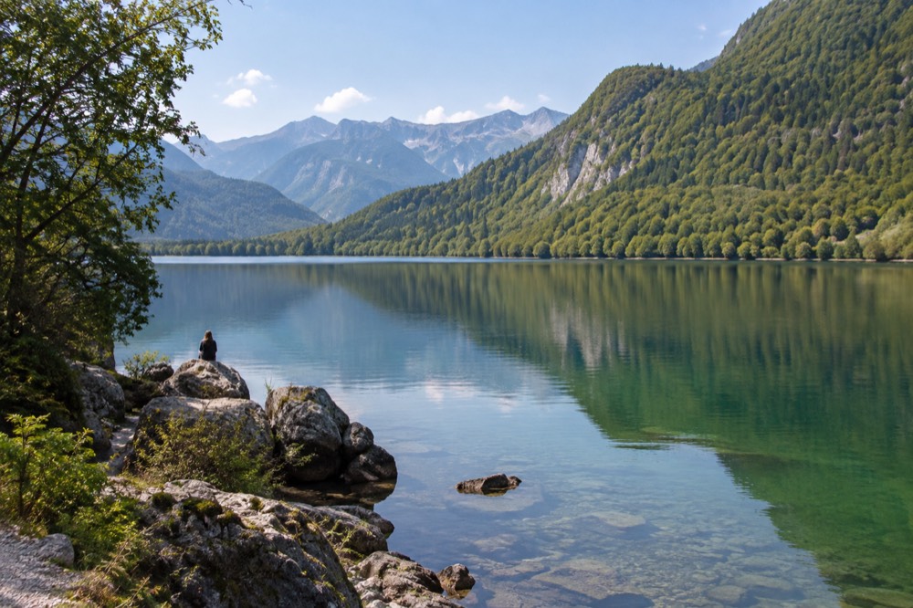Still turquoise water of Lake Bohinj with forested hills reflected on the surface and mountains behind