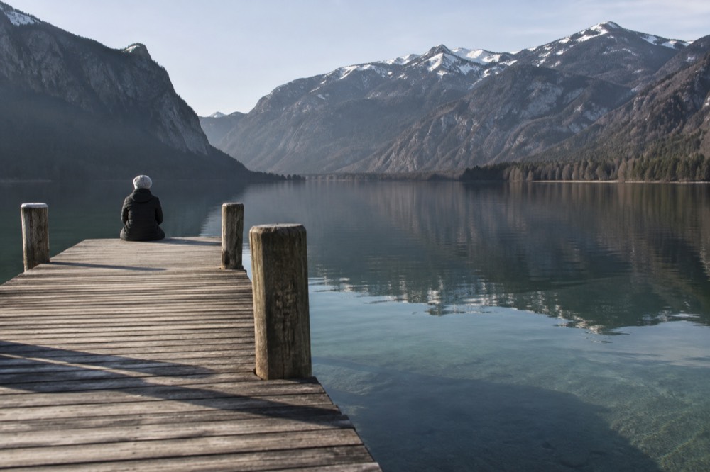 A wooden jetty over clear green lake water with mountains reflected in the calm surface