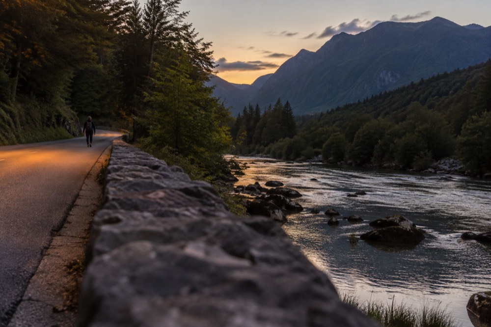 A winding mountain road beside a river with steep forested slopes in evening light