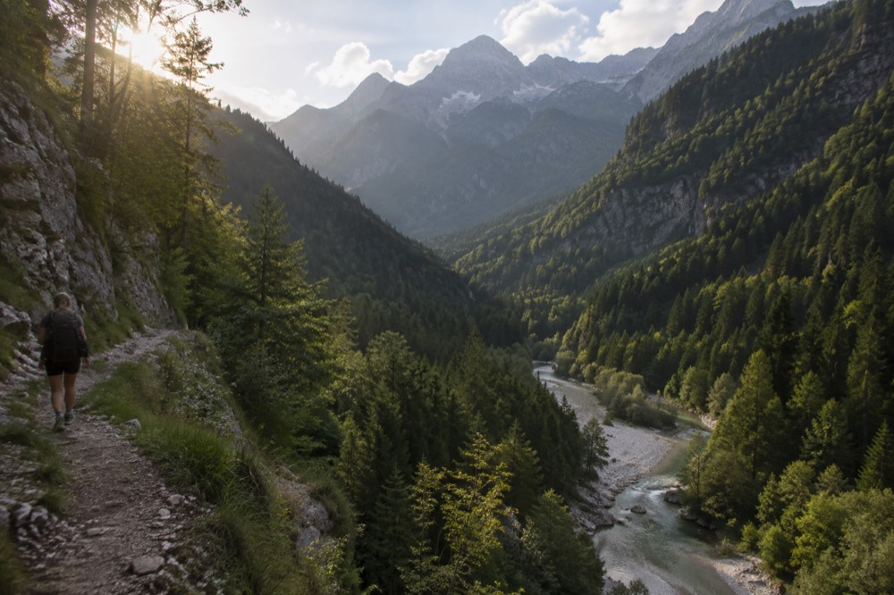 An emerald river running through a steep green alpine valley with high peaks behind