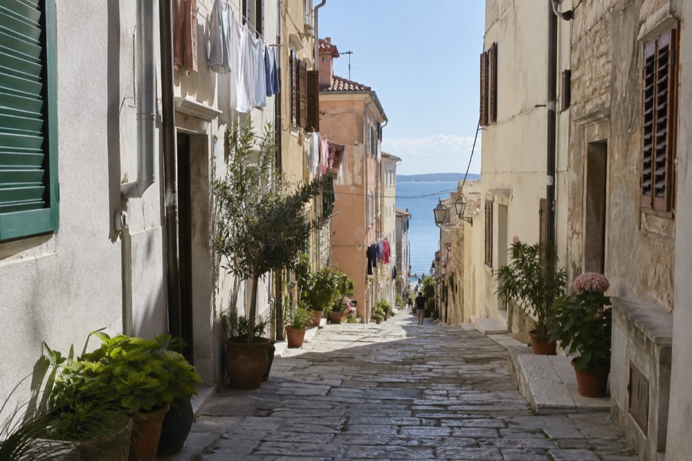 Narrow stone street in Piran old town with shuttered facades and laundry lines