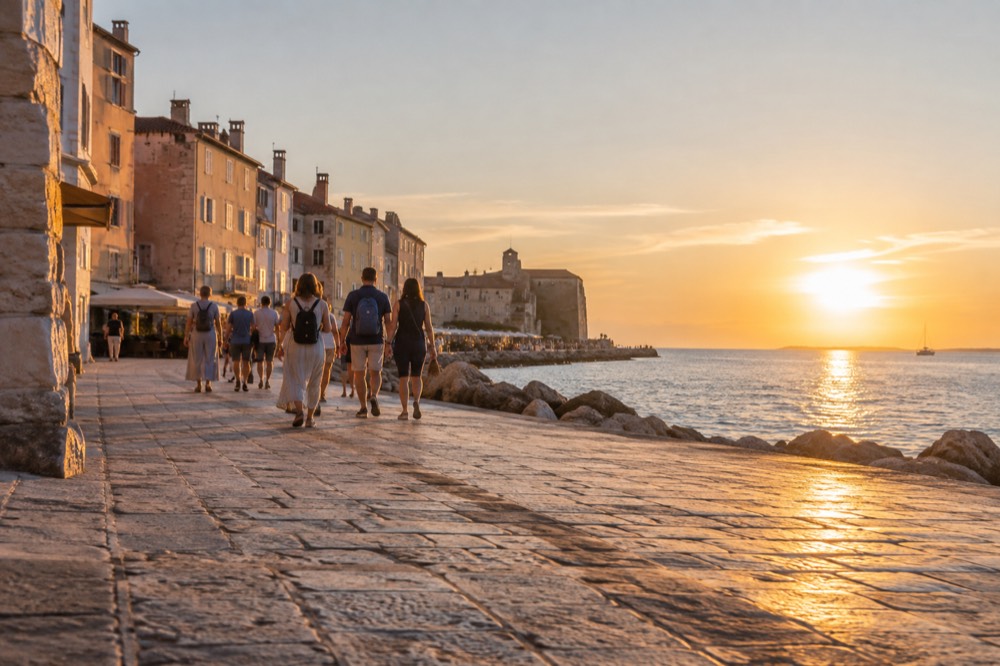 Guided walking group on a sunlit stone square near the Piran waterfront