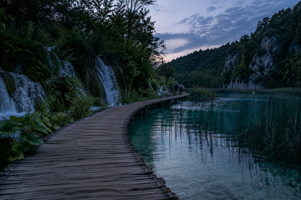 Boardwalk path crossing turquoise water between forested banks at Plitvice Lakes