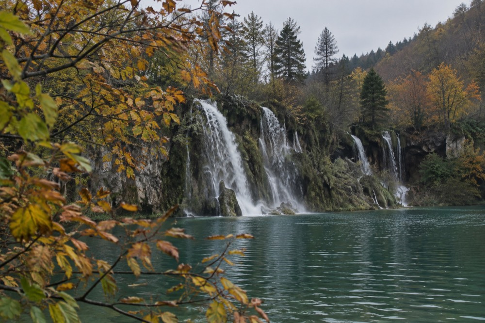 Waterfall pouring between autumn trees into a green lake at Plitvice Lakes