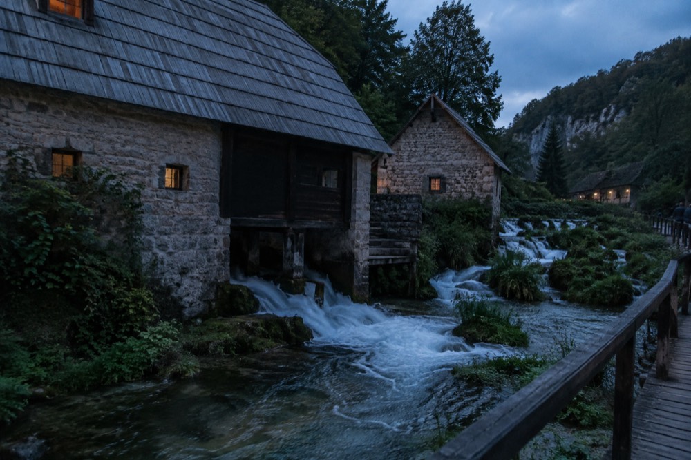 Stone watermill buildings beside a small river with waterfalls running beneath them