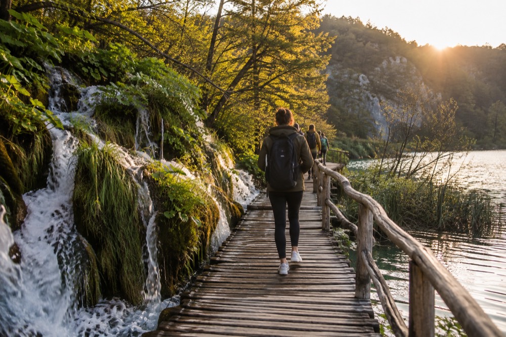 Tourists on a wooden walkway above clear water with small waterfalls on either side