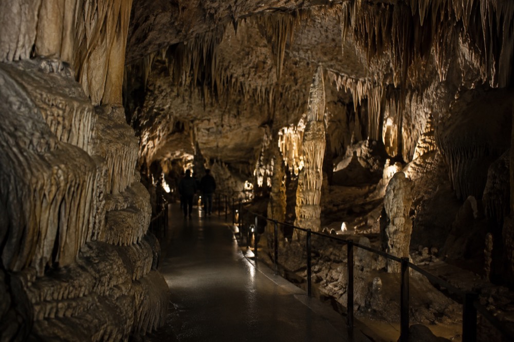 Walkway through a lit stalactite passage inside a limestone cave