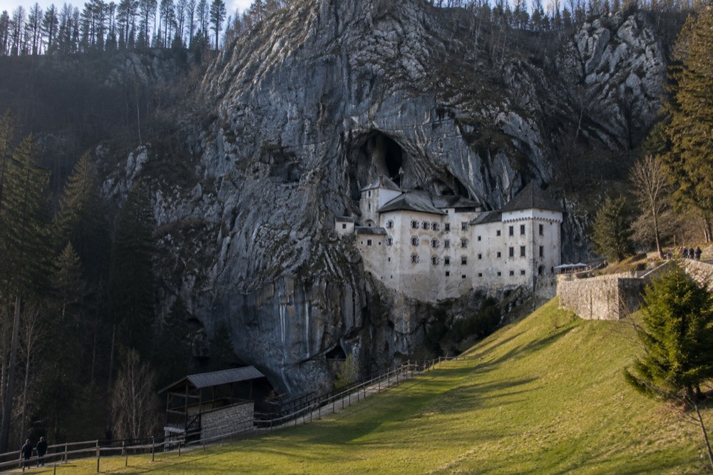 A green meadow below a tall cliff with a castle built into the rock face