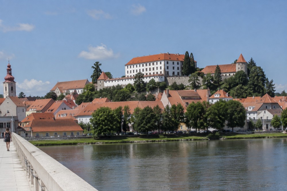 A stone castle on a hill overlooking a wide river and red rooftops