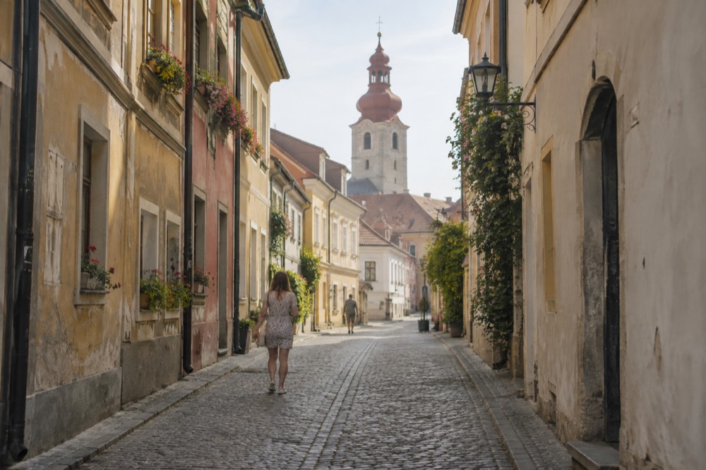 A narrow old street with pastel facades, window boxes and a church tower beyond