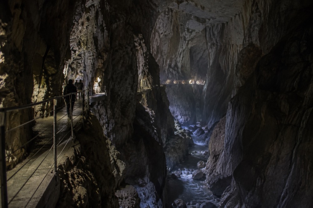 A narrow walkway clinging to the rock wall inside a large dimly lit cave chamber