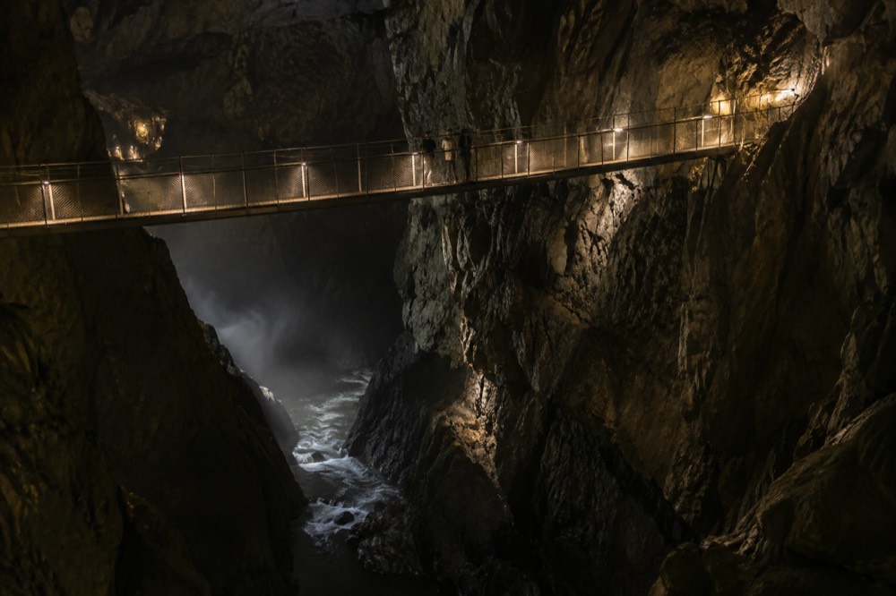 A suspension bridge high above an underground river in a vast dark cavern