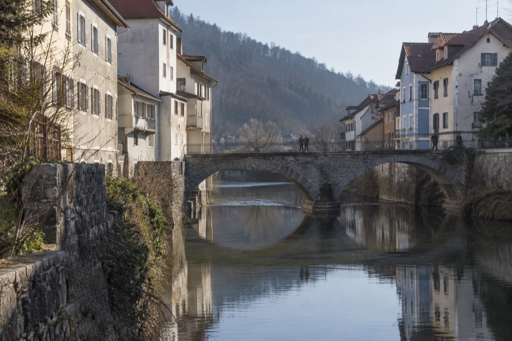 A stone bridge over a calm river with medieval houses reflected in the water