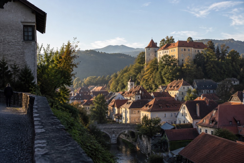 A stone castle on a wooded hill overlooking a small town of red rooftops