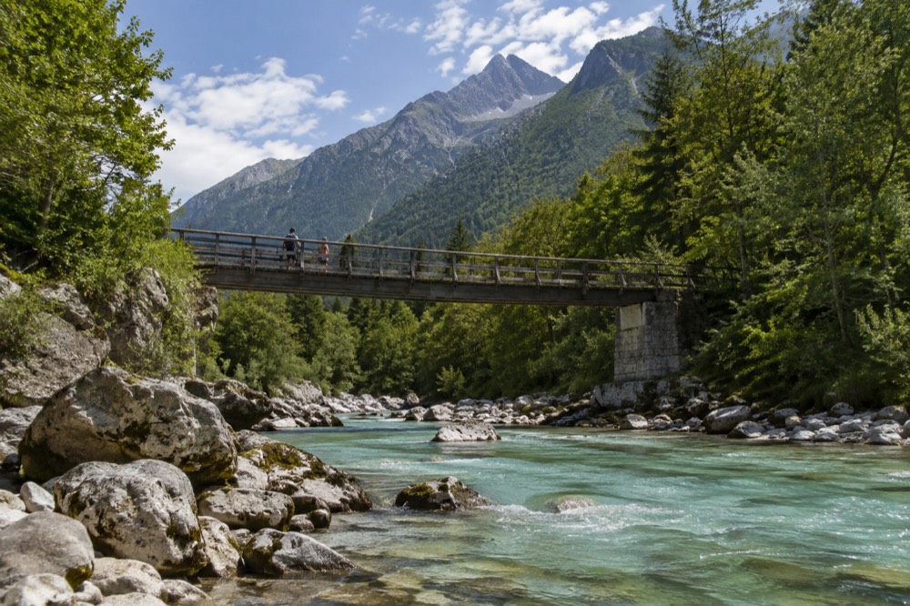 A wooden bridge crossing the green Soča River with mountains rising behind it