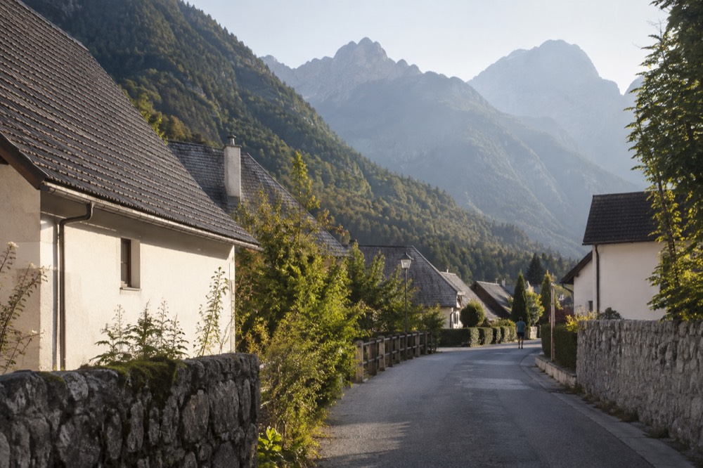A quiet alpine village street in late afternoon light with forested slopes behind the roofs