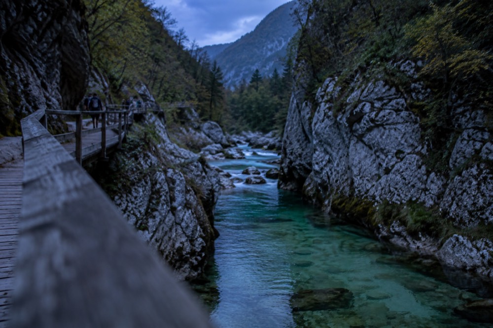 Wooden walkway along a narrow river gorge with clear green water between rock walls