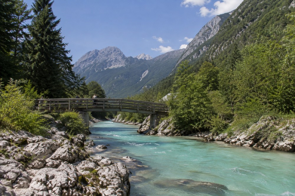 Narrow alpine valley with a wooden bridge over a bright turquoise river