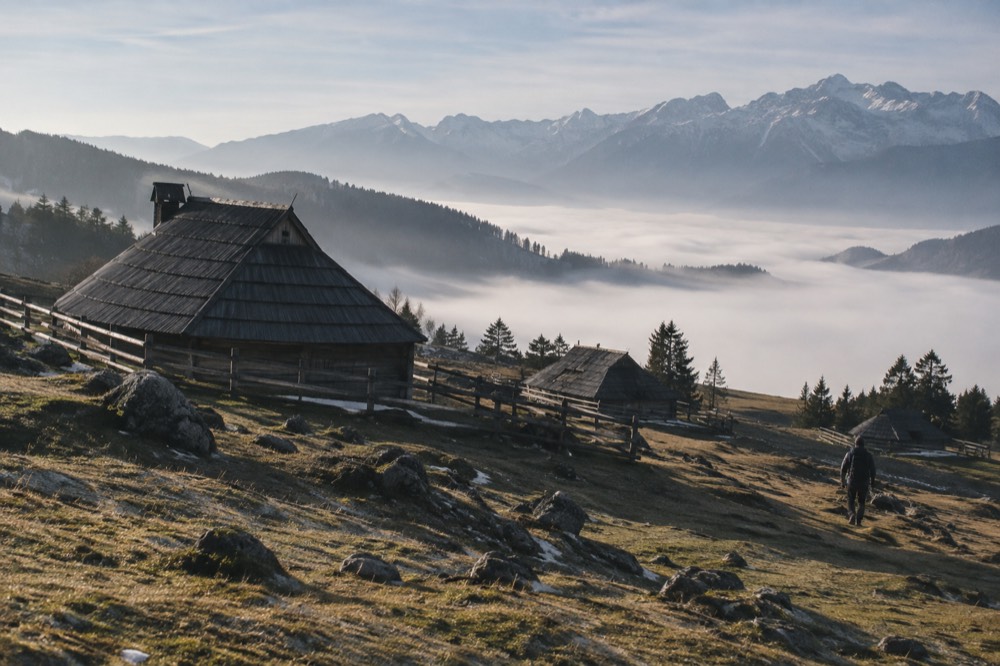 Morning fog filling a valley below a sunlit alpine meadow edge