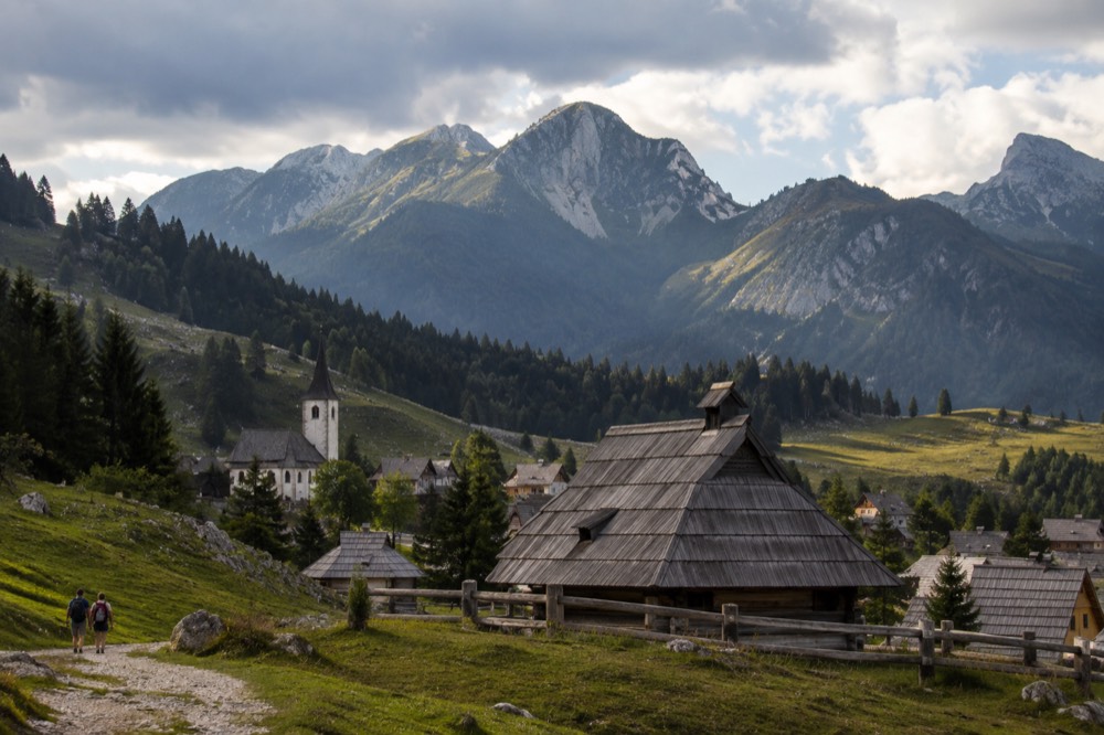 A small alpine town with a church tower beneath forested hills and mountains