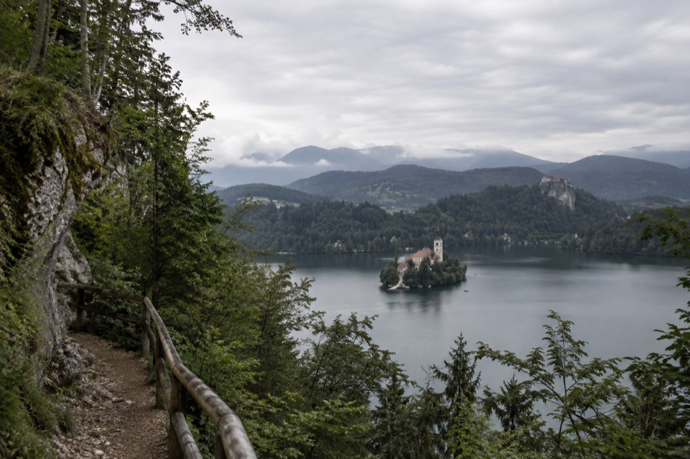 A calm alpine lake with a church on a small island and a castle on a cliff above it