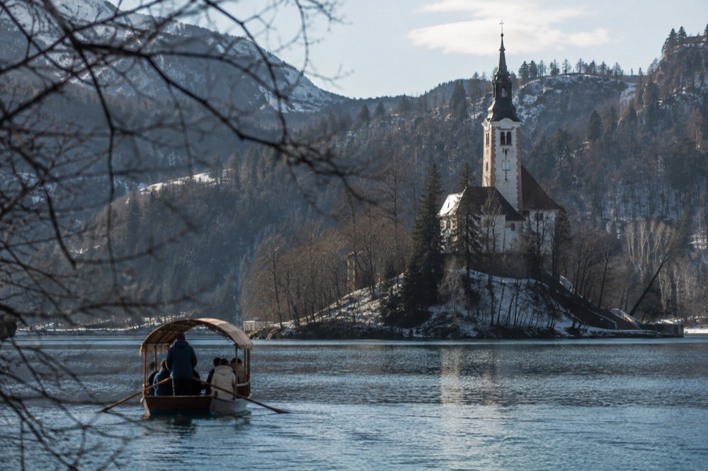 A traditional wooden boat crossing a lake towards a small island with a church tower