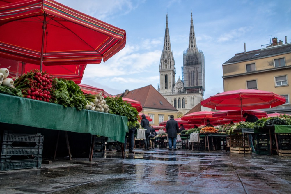 Red market umbrellas and fresh produce stalls in a city market square