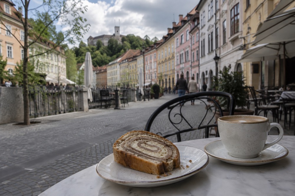 Sliced potica roll with walnut filling on a ceramic plate beside a coffee cup